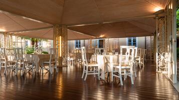 Un comedor interior con varias mesas y sillas, suelo de madera y una gran estructura similar a una carpa en el techo.