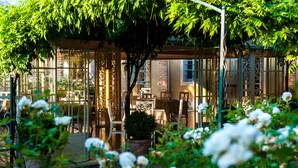 A cozy outdoor seating area with tables and chairs, surrounded by lush greenery and white flowers. - Hotel Il Campanile (Cherasco)