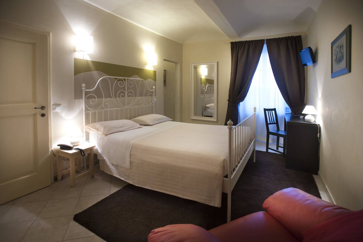A bedroom with a bed, bedside table, lamp, chair, and a small desk.