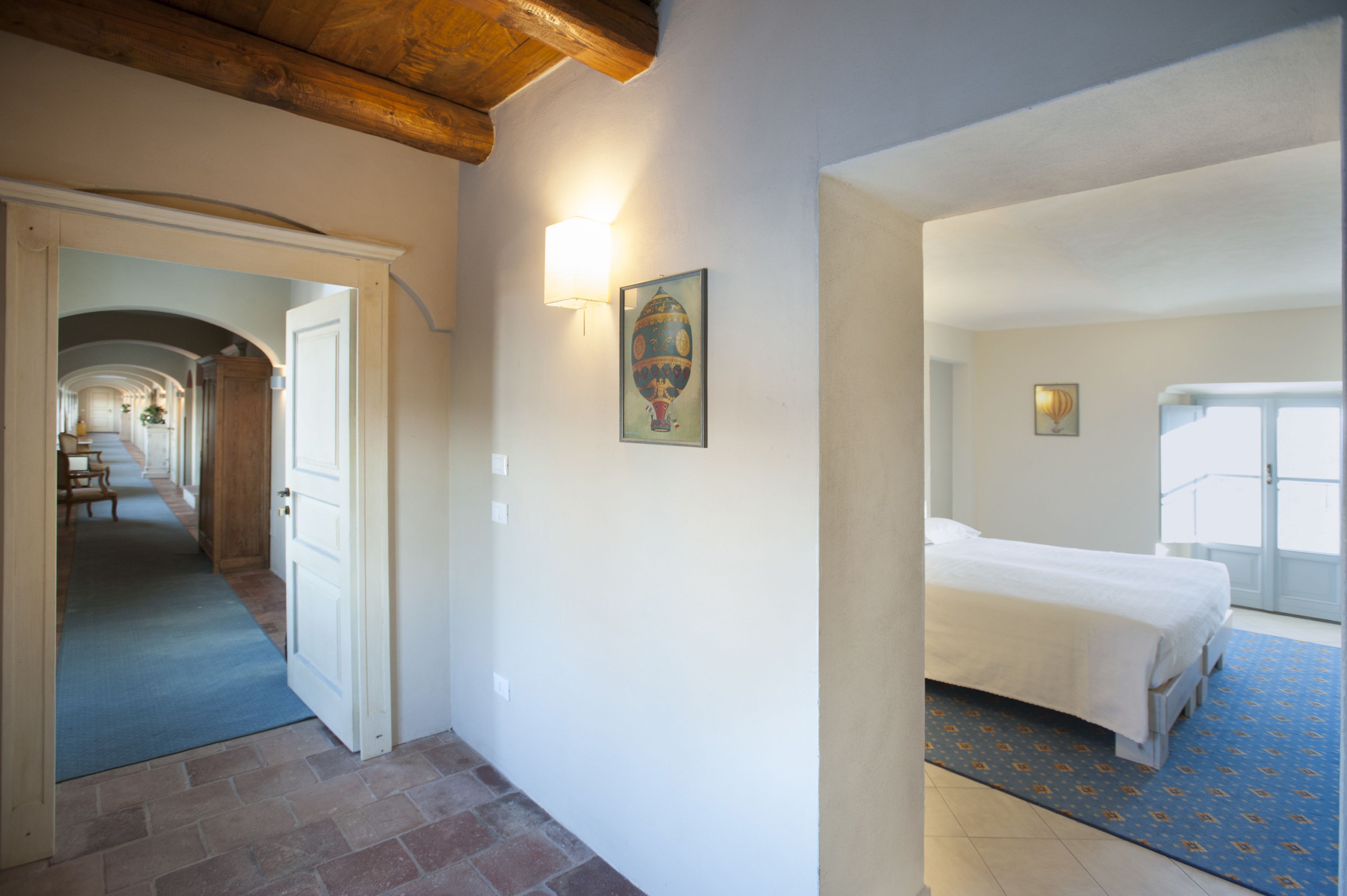A hotel room with a bed, a blue patterned rug, and a hallway leading to a dining area.
