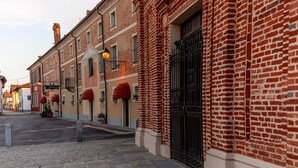 A street with traditional brick buildings, a cobblestone sidewalk, and a black wrought iron gate. - Hotel Il Campanile (Cherasco)