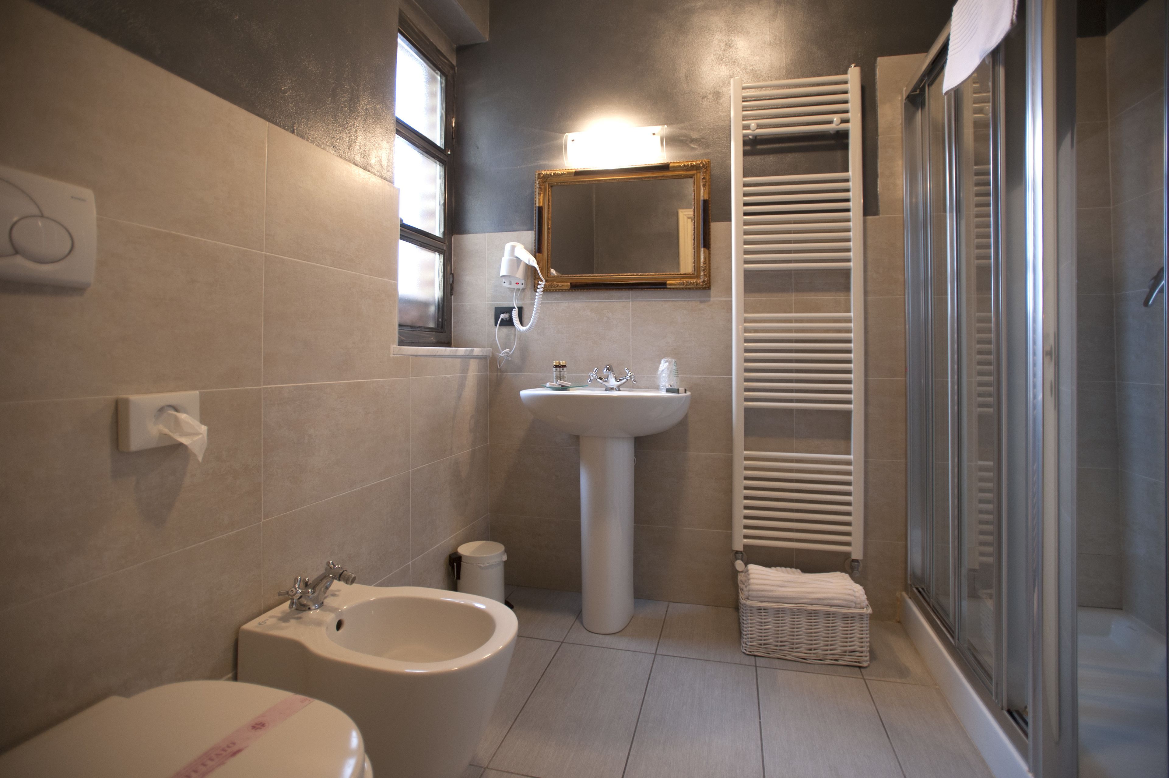 Een moderne badkamer met een wastafel op voet, een toiletbrons, een toilet, een spiegel en een douche met glazen wanden.