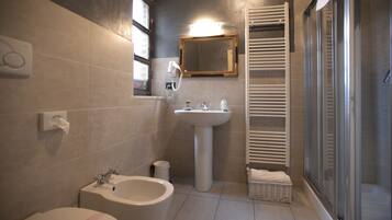 Een moderne badkamer met een wastafel op voet, een toiletbrons, een toilet, een spiegel en een douche met glazen wanden.