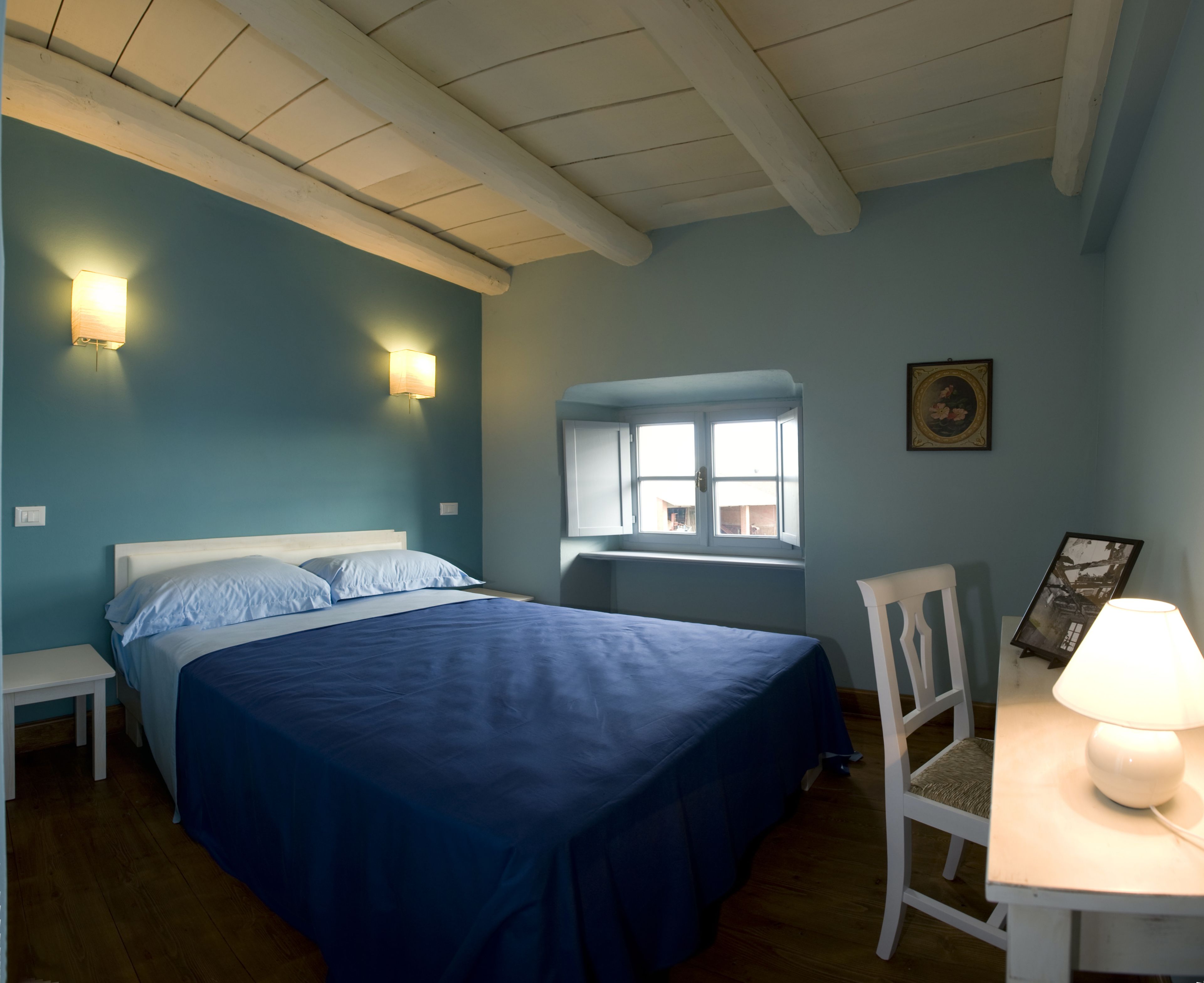 A bedroom with a bed, bedside tables, a window, and a desk with a lamp.