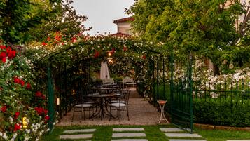Uma área de jardim externa com um caminho que leva a um espaço de estar com mesas e cadeiras.