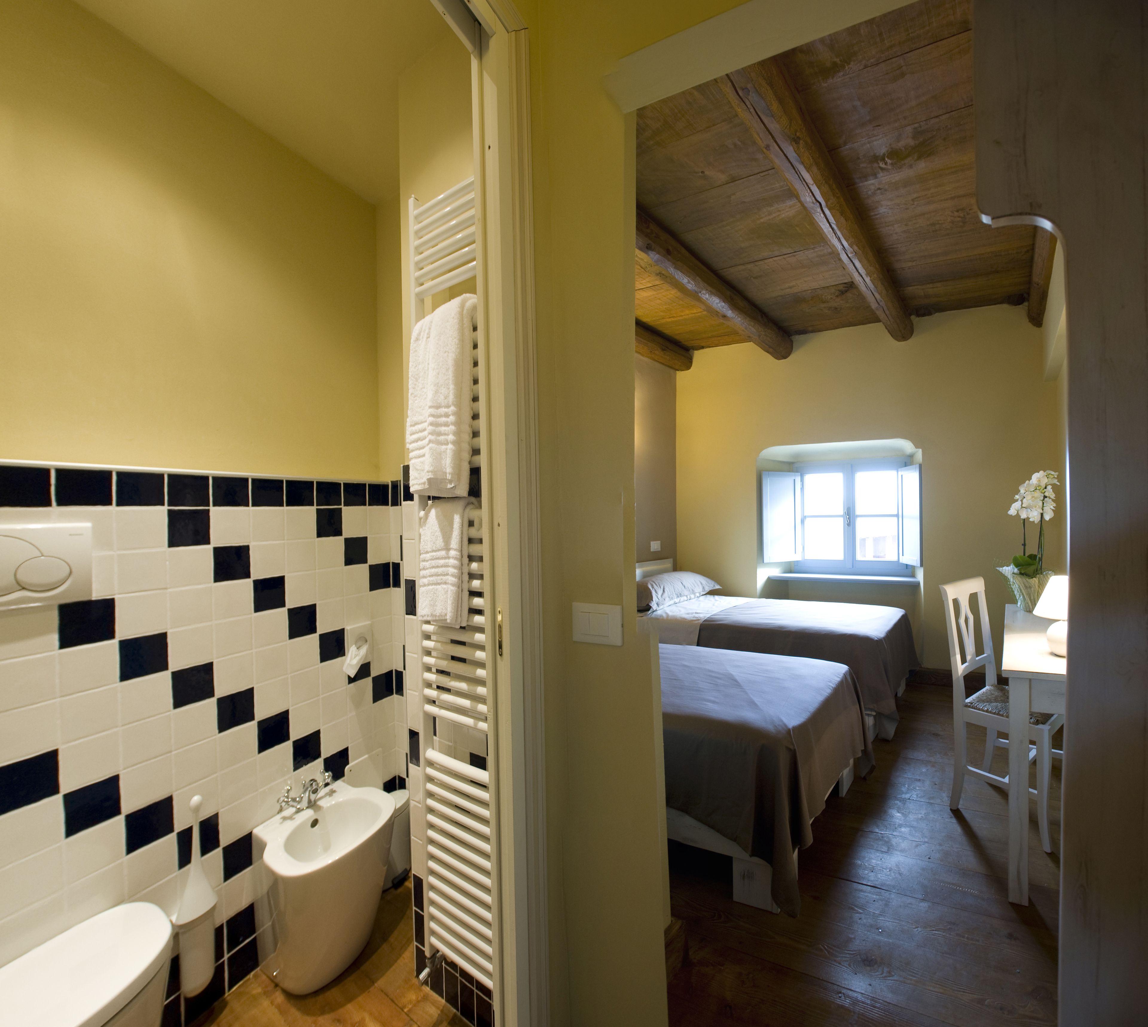 Ein Badezimmer mit Toilette, Waschbecken und Handtuchhalter. Im angrenzenden Raum befindet sich ein Bett mit einem Fenster.