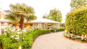 A garden pathway leading to a conservatory with a palm tree and white flowers. - Hotel Il Campanile (Cherasco)