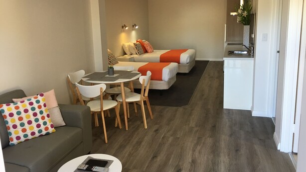 Una sala de estar moderna con un sofá, una mesa de comedor con sillas, una zona de cocina y un televisor pequeño montado en la pared.