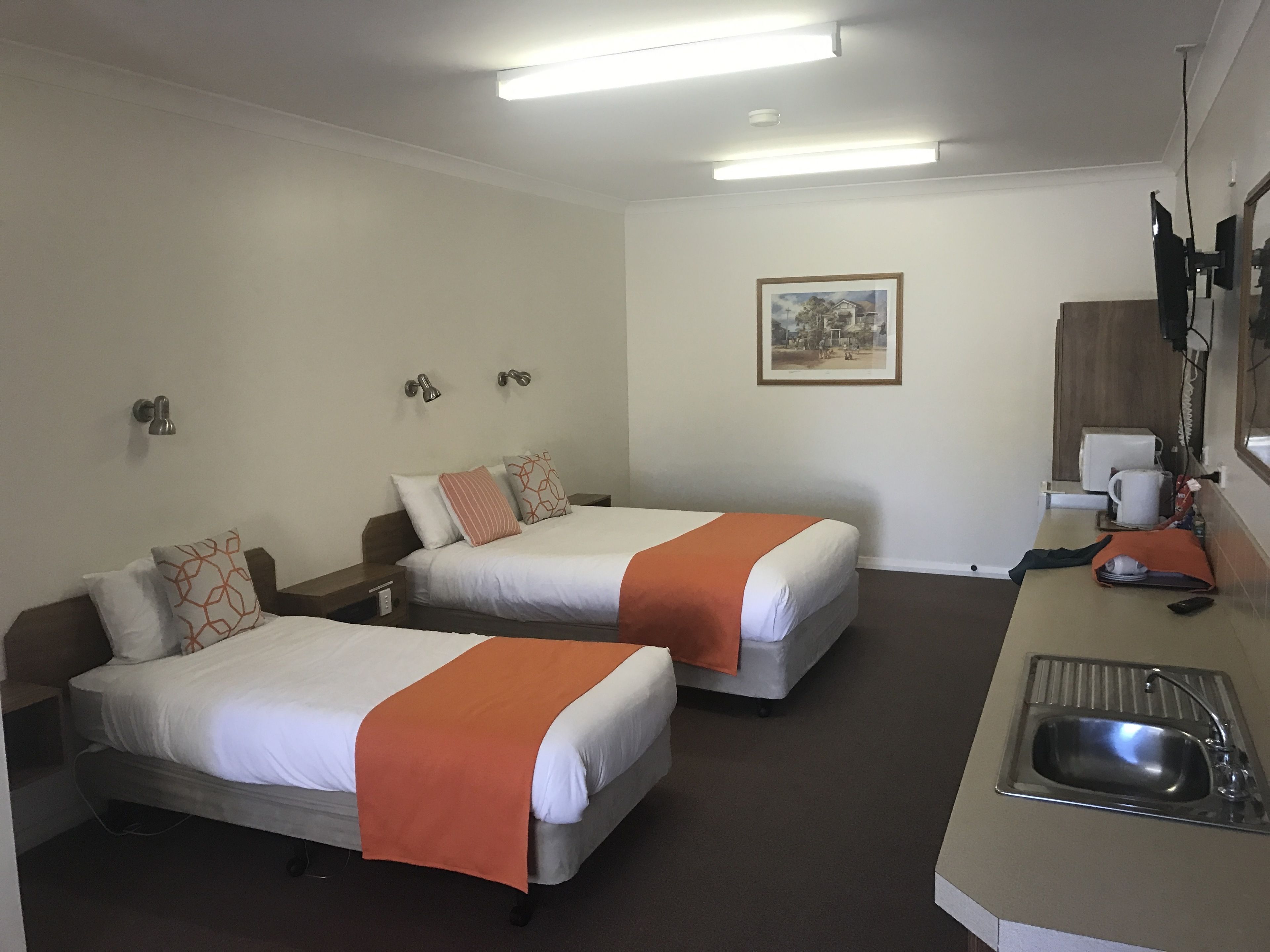 Quarto de hotel com duas camas, uma kitchenette pequena, uma pia e um quadro emoldurado na parede.