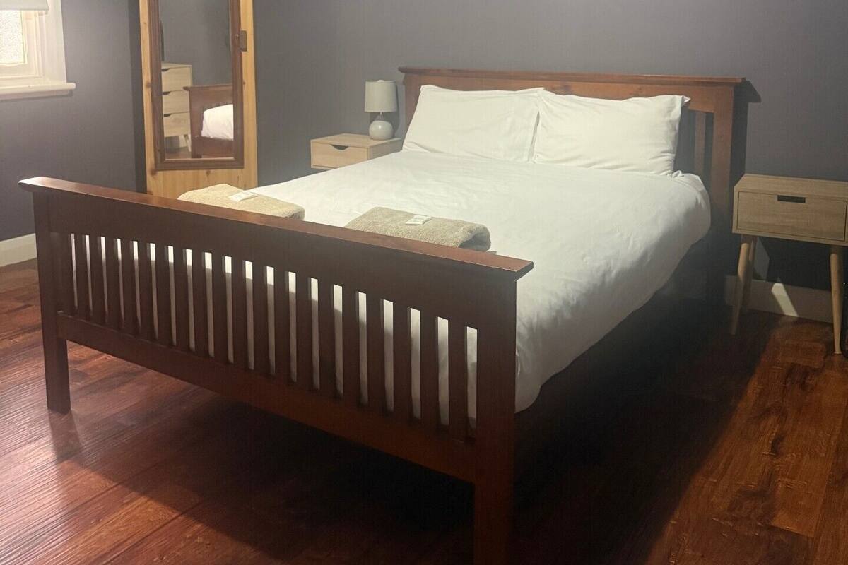 A bedroom with a wooden bed, a nightstand, a bedside table, and a mirror.