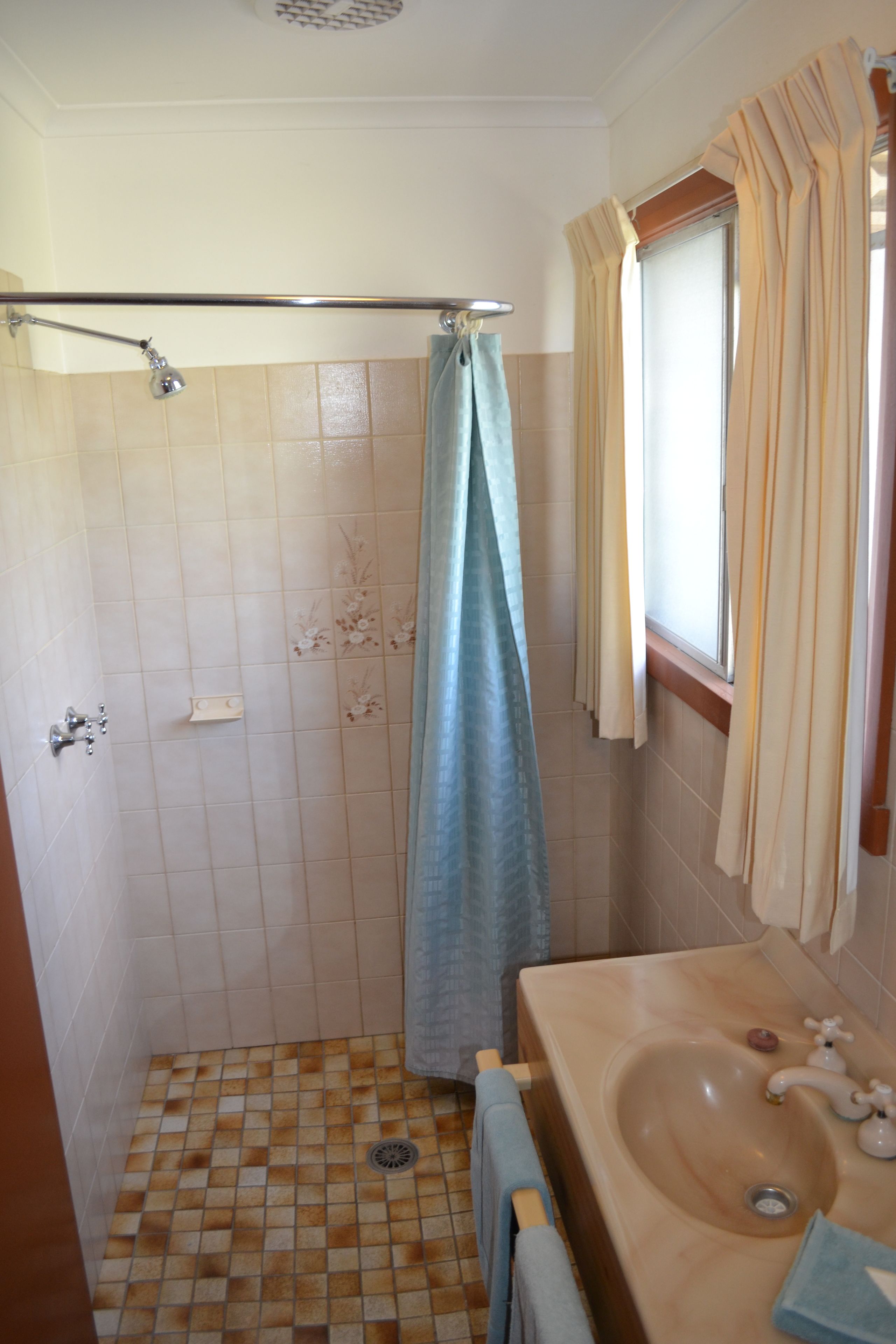 Un baño con ducha, lavamanos y ventana con cortinas.