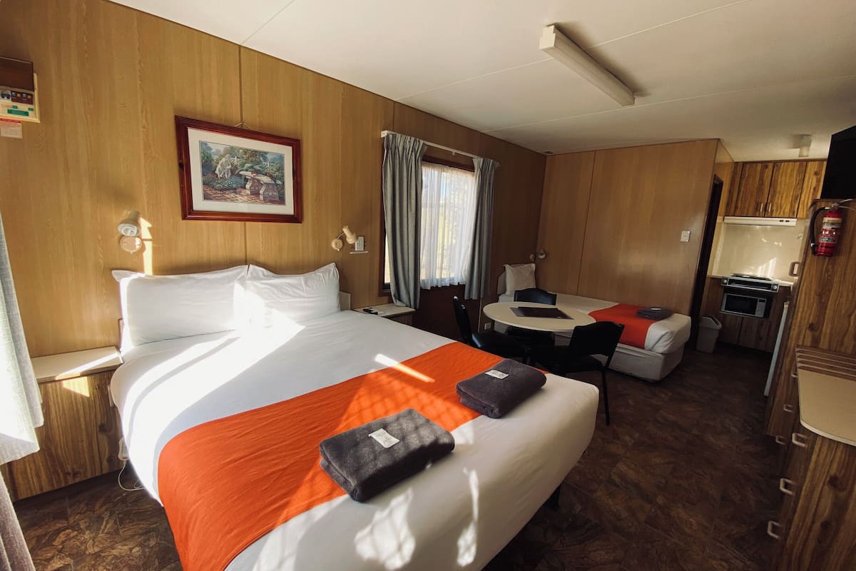 A hotel room with a bed, a desk, a chair, a small table, and a microwave.
