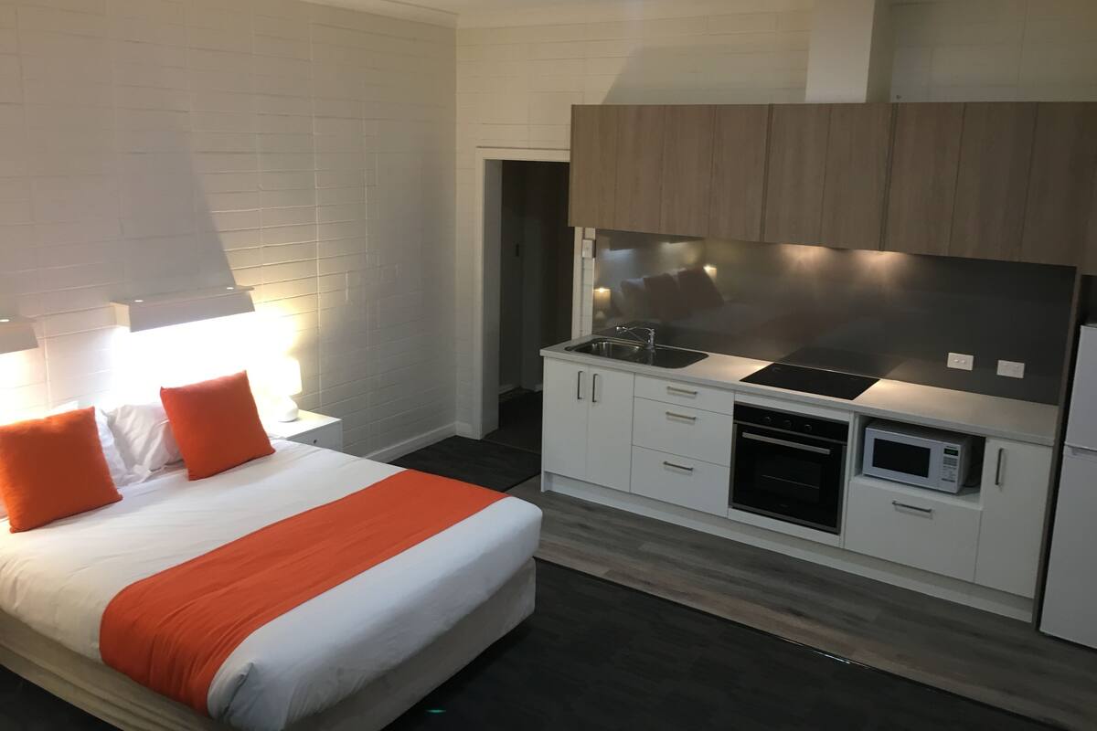 A modern hotel room with a bed, a kitchenette, and a bathroom.