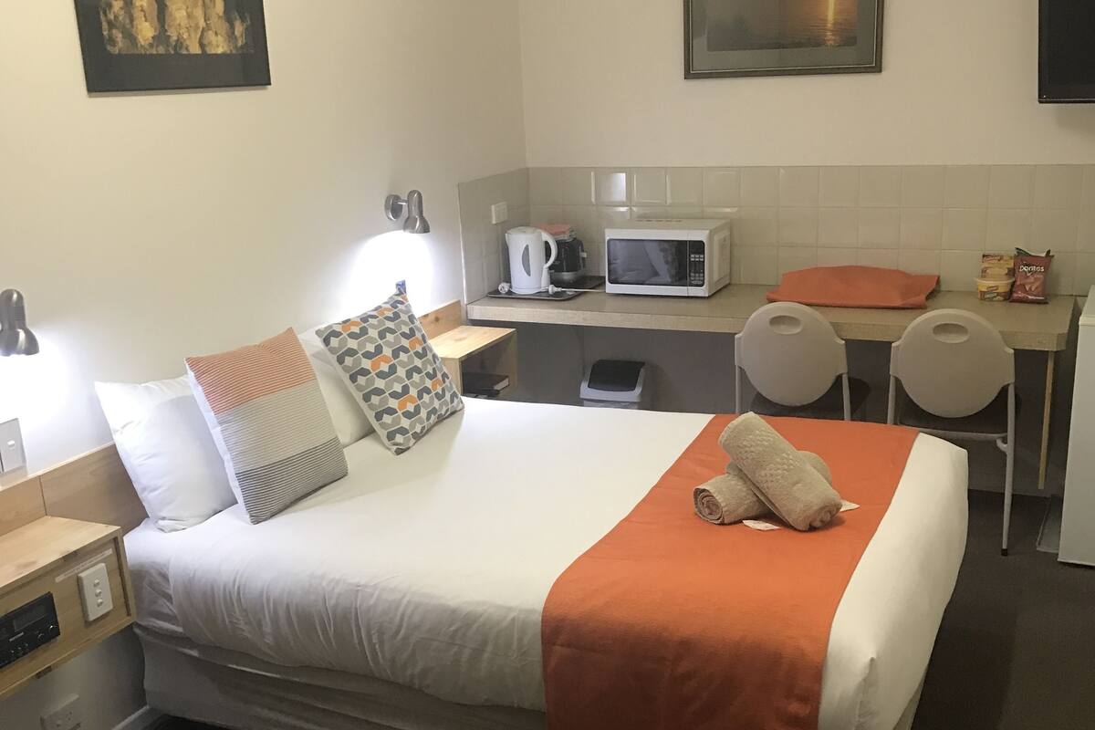 A hotel room with a bed, a desk, a microwave, and a small kitchen area.