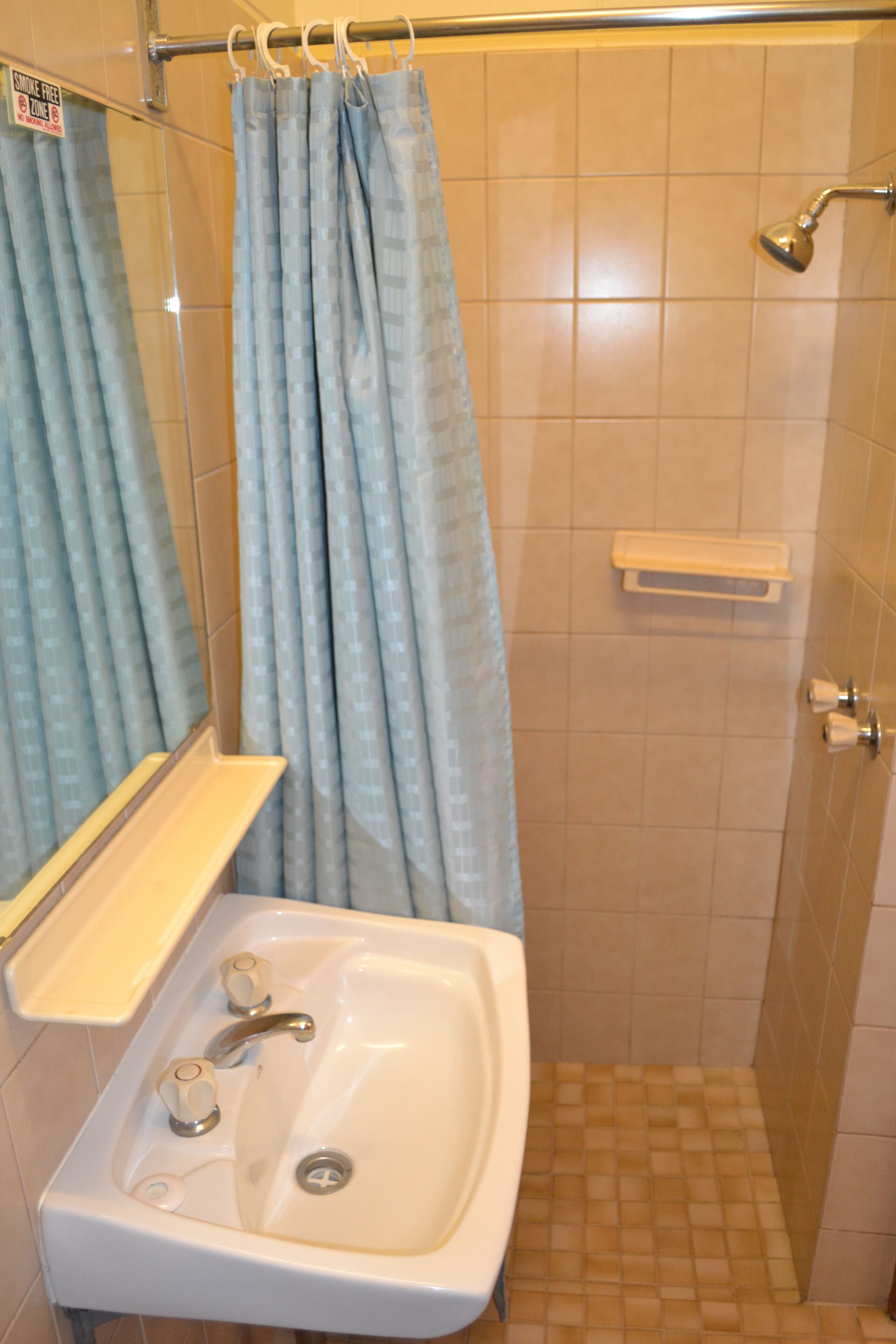 Une salle de bain avec un lavabo, un miroir, un rideau de douche et des murs carrelés.
