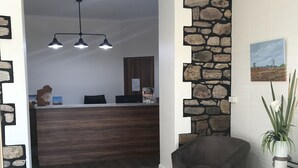 Zona de recepción con un muro decorativo de piedra, un mostrador de madera y un sillón gris.