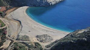 An aerial view of a coastal area with a sandy beach, a clear blue sea, and rocky cliffs.