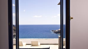 An open window with a view of the sea and a patio with chairs.