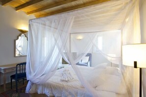 A bedroom with a canopy bed, a desk with a chair, and a lamp. - Aegea Blue Cycladic Resort (Andros)