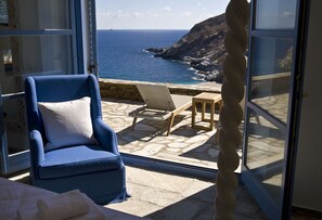 Ein Zimmer mit Meerblick, ein blauer Sessel, ein kleiner Tisch und ein Steinfußboden.