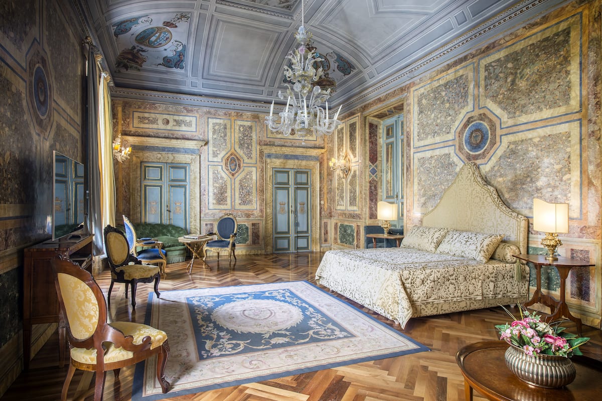 A luxurious bedroom with a large bed, ornate ceiling, and classic furniture.