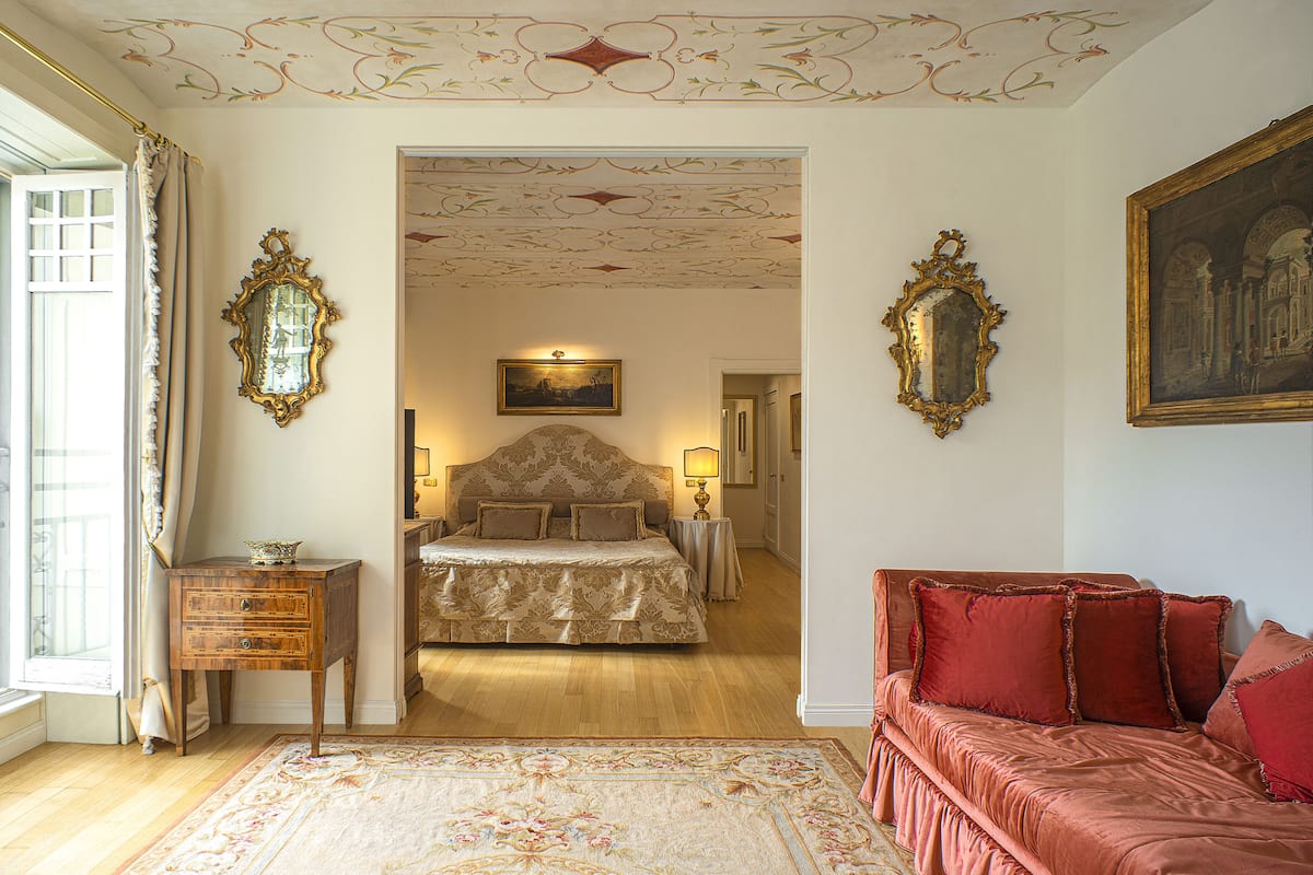 A bedroom with a large bed, a red sofa, and ornate ceiling decorations.