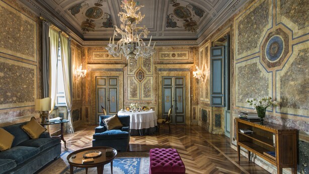 Ein luxuriöses Zimmer mit einer Kristallleuchter, einer verzierten Decke und einem Essbereich mit Tisch für vier Personen.