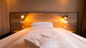 A neatly made bed with a white comforter and pillows, two bedside lamps, and a wooden headboard. - HotelSportforum (Rostock)