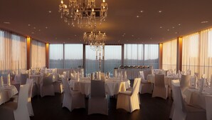 A banquet hall with round tables, white chairs, and a large chandelier. - HotelSportforum (Rostock)
