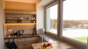A modern kitchen with wooden cabinets, a sink, and a window overlooking a snowy landscape. - HotelSportforum (Rostock)