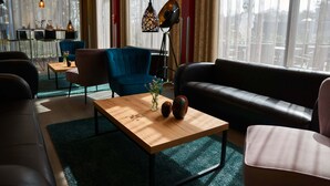 A modern living room with a wooden coffee table, a blue armchair, a black sofa, and a floor lamp. - HotelSportforum (Rostock)