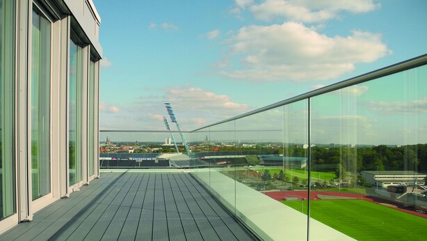A modern building with a glass balcony overlooking a sports field and distant cityscape. - HotelSportforum (Rostock)