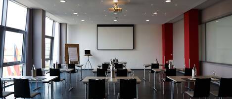 Une salle de conférence équipée de tables, de chaises, d’un écran de projection et d’un tableau blanc.