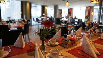 A dining area with tables set for two, featuring red placemats, white tableware, and decorative napkins.