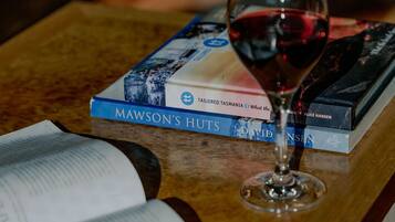 A glass of red wine on a wooden table with a book titled "Mawson's Huts" and another book by David Nissen.