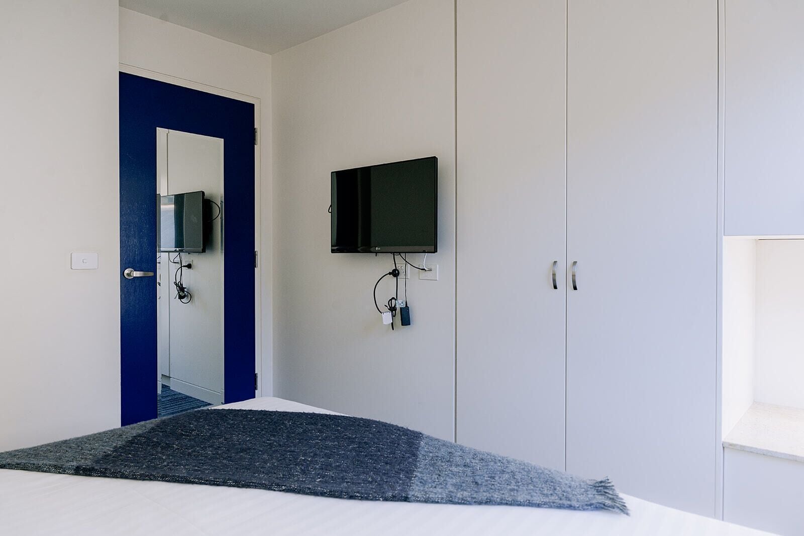 A bedroom with a bed, a TV mounted on the wall, and a wardrobe.