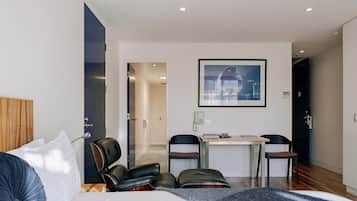 A hotel room with a bed, two chairs, a small table, a phone, and a framed picture on the wall.