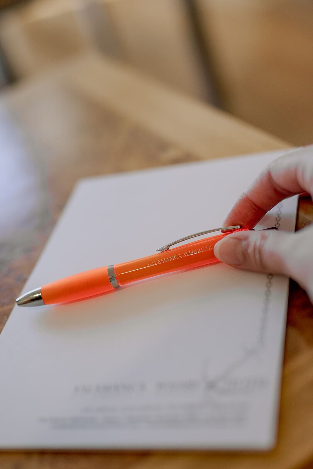A hand holding a pen with the text "SALAMANCA WHARF HOUSE" on a piece of paper.