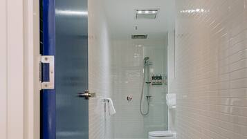Un baño estrecho con paredes de azulejos blancos, una puerta azul, una ducha y un inodoro.