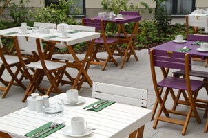 Un comedor con mesas y sillas blancas y púrpuras, dispuesto con platos, tazas y cubiertos.