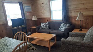 A cozy room with wooden walls, a sofa, a patterned armchair, a dining table, and two lamps. - Mayfield Country Cottages (Mayfield)