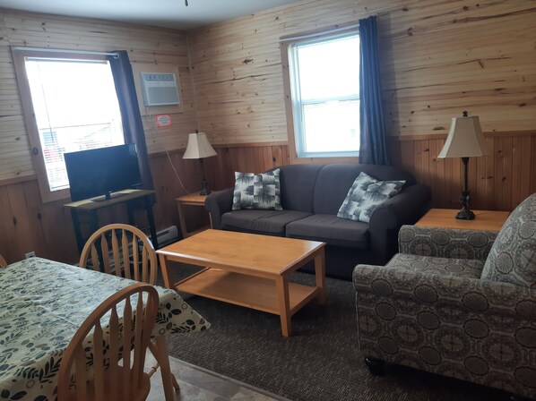 A cozy room with wooden walls, a sofa, a patterned armchair, a dining table, and two lamps. - Mayfield Country Cottages (Mayfield)