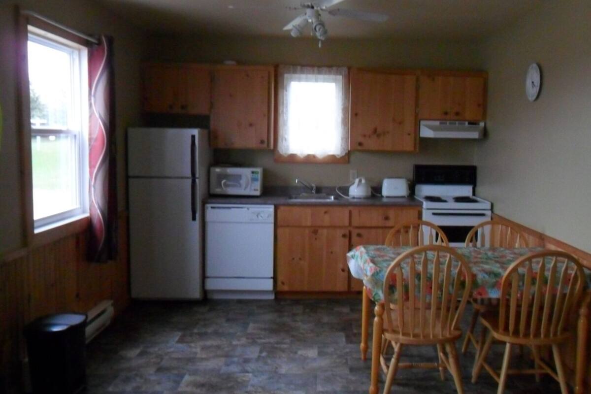 A compact kitchen with wooden cabinets, a refrigerator, a microwave, a stove, and a dining table with chairs.