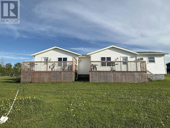 Two white mobile homes with attached porches, fenced in, and surrounded by a grassy field.