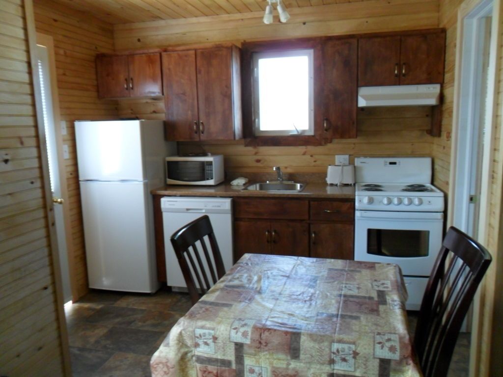 Une cuisine compacte dotée de meubles en bois, d’un réfrigérateur, d’un four à micro-ondes, d’un lave-vaisselle, d’une cuisinière et d’une table à manger avec des chaises.