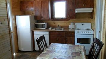 Une cuisine compacte dotée de meubles en bois, d’un réfrigérateur, d’un four à micro-ondes, d’un lave-vaisselle, d’une cuisinière et d’une table à manger avec des chaises.
