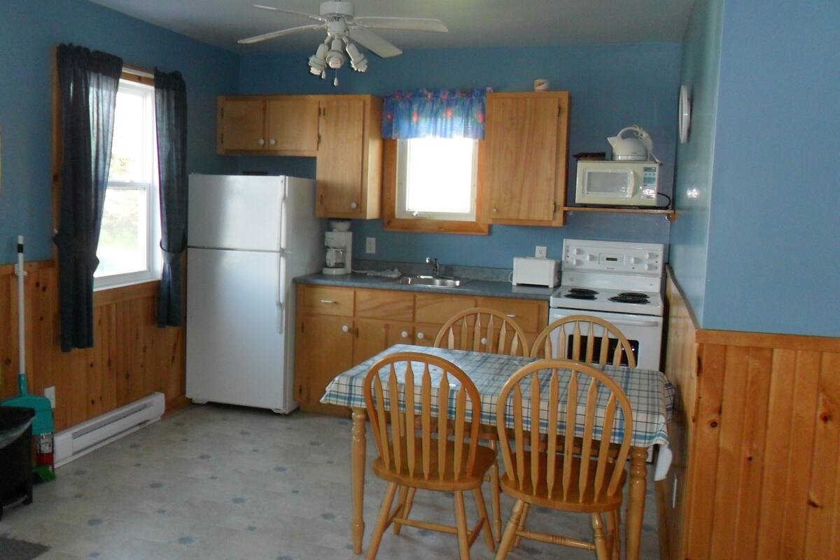 A compact kitchen with wooden cabinets, a refrigerator, a microwave, a stove, and a dining table with chairs.