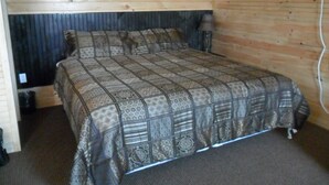 A wooden-paneled room with a bed, a nightstand, and a lamp. - Mayfield Country Cottages (Mayfield)