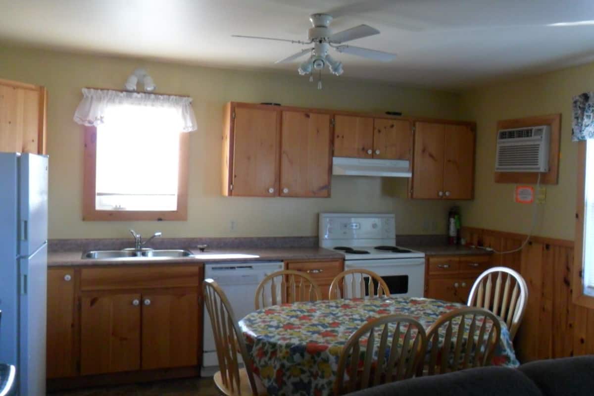 A compact kitchen with wooden cabinets, a stove, a sink, and a dining table with chairs.