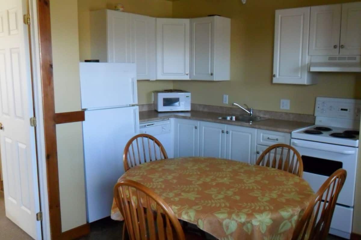 A compact kitchen with white cabinets, a microwave, a sink, and a stove. There is a dining table with four chairs.